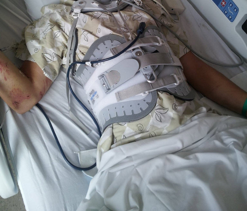 Hospital bed after a severe motorcycle accident — cervical collar and full back brace, road rash on the arm